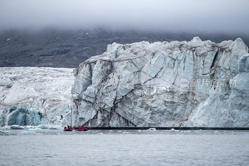 海神号(Poseidon Expeditions)探险游轮上的乘客乘坐一艘Zodiac摩托化橡皮艇，近距离观看高耸的冰川墙